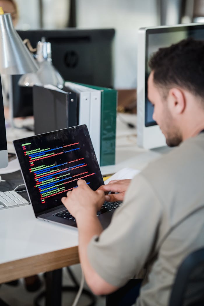 hero-img-02 Focused software developer typing code on a laptop in a modern office setting.