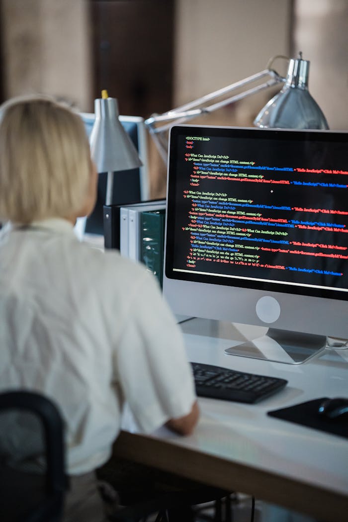 about-01 Professional woman coding at office desk with two monitors and desk lamps.